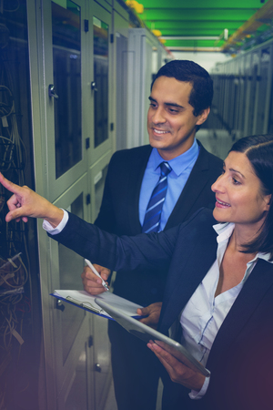Technicians interacting with each other while analyzing server in server roomの写真素材