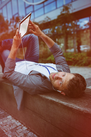 Business executive listening music on digital tablet while lying on retaining wallの写真素材