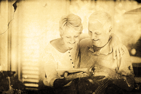 Grey background against happy senior couple holding digital tablet while standingの写真素材