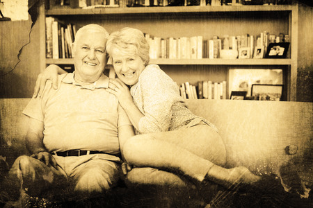 Grey background against portrait of happy senior couple sitting on sofa against bookshelfの写真素材