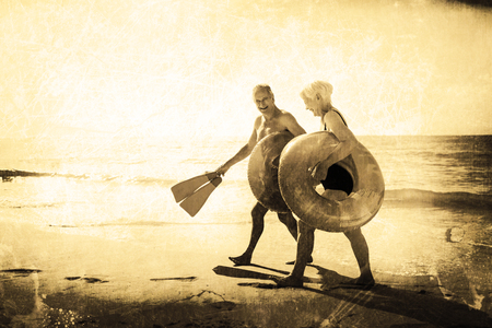 Grey background against happy senior couple walking on beachの写真素材