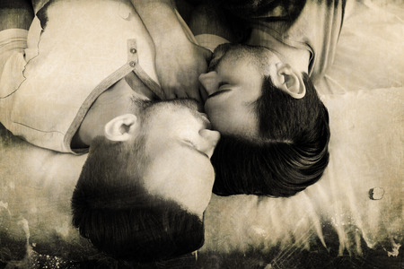 Grey background against happy gay couple lying on bedの写真素材