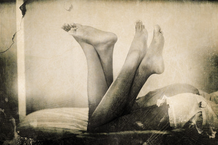 Grey background against side view of couple on bed with raised legsの写真素材