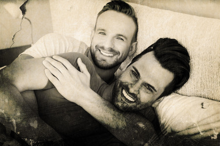 Grey background against happy gay couple lying on bedの写真素材