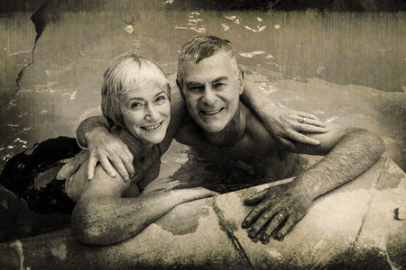 Grey background against portrait of happy senior couple in poolの写真素材