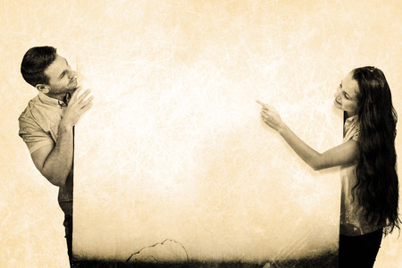 Smiling couple pointing on white sheet against grey backgroundの写真素材