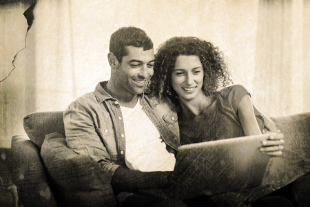 Grey background against young couple using laptop while sitting on sofa