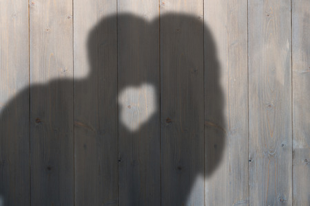 Man kissing woman on cheek against pale grey wooden planksの写真素材