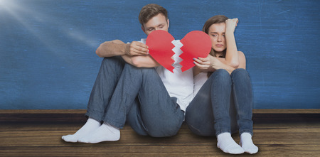 Young couple holding broken heart against blue room
