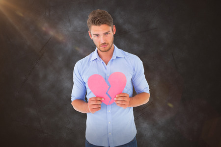 Sad man holding a broken heart against greyの写真素材