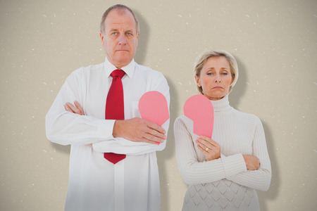 Older couple standing holding broken pink heart against creamの写真素材