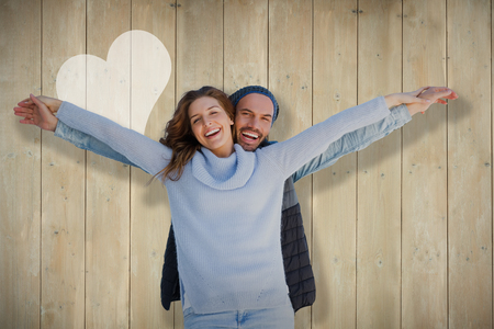 Happy couple standing with arms outstretched against wooden planksの写真素材