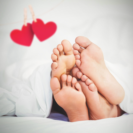 Hearts hanging on a line against feet sticking out from blanketの写真素材