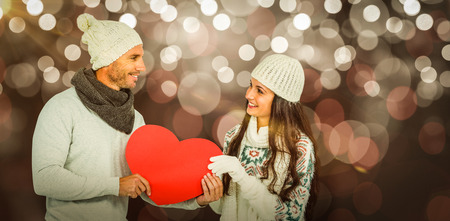 Smiling couple holding paper heart against glowing background