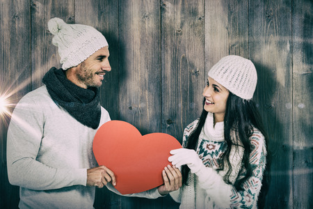 Smiling couple holding paper heart against pale grey wooden planksの写真素材