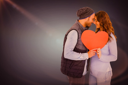 Happy young couple holding heart shape paper against blue vignette backgroundの写真素材