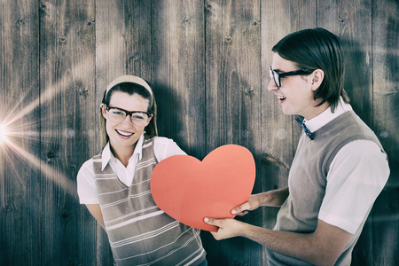 Geeky hipster offering red heart to his girlfriend  against pale grey wooden planksの写真素材