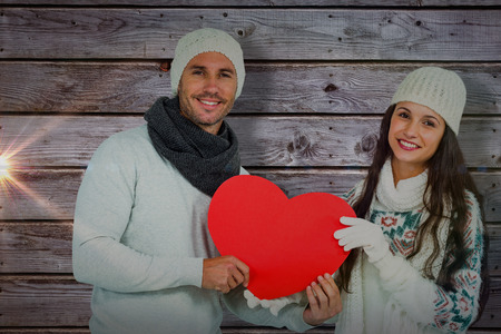 Smiling couple holding paper heart against digitally generated grey wooden planksの写真素材