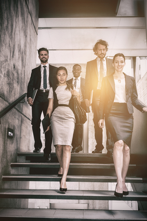 Confident businesswoman with colleagues climbing stairs in officeの写真素材