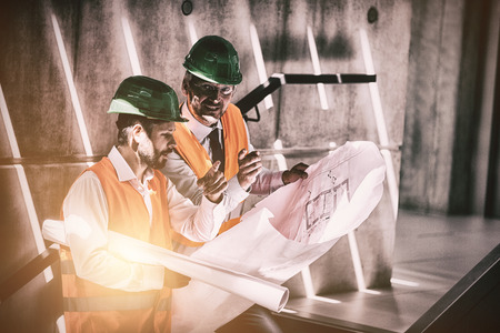 Architects standing on staircase discussing with blueprint in office building
