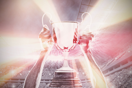 Cropped hand of athlete holding trophy against football stadiumの写真素材