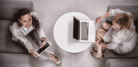 Overhead view of businesswomen using laptop and digital tablet in officeの写真素材