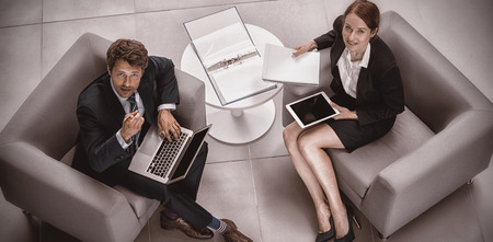 Overhead view of businessman and colleague holding laptop and digital tablet in officeの写真素材