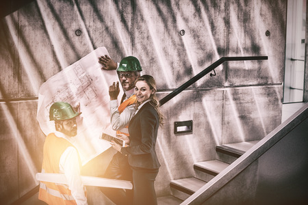 Happy businesswoman and architects standing on a staircase discussing with blueprint in office buildingの写真素材