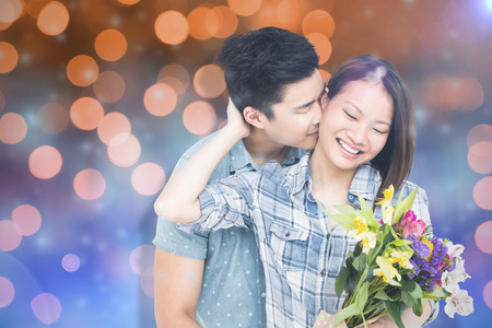 Man kissing woman with bouquet against glowing backgroundの写真素材