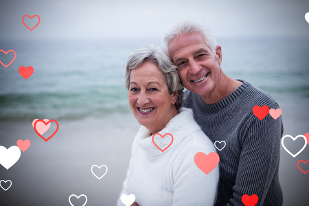 Valentines heart design against portrait of happy senior couple embracing at beach 3dの写真素材