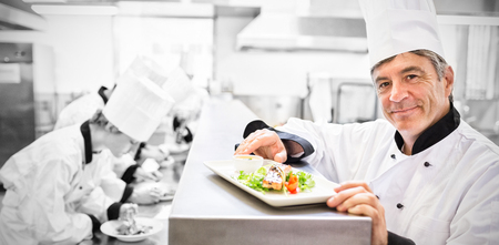 Trainees preparing dishes with head chef presenting salmon dish on counterの写真素材