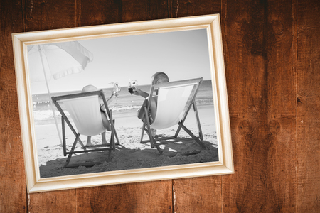 Happy couple drinking cocktails while relaxing on their deck chairs against weathered oak floor boards backgroundの写真素材