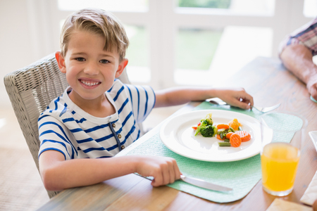 Cute boy having meal on dinning table at homeの写真素材