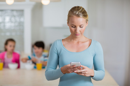 Beautiful woman using mobile phone in kitchen at homeの写真素材