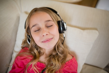 Cute girl lying on sofa and listening to music on headphones in living room at homeの写真素材