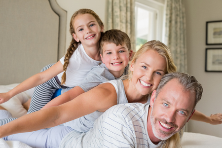 Portrait of happy family stacking on top of each other on the bed in bedroomの写真素材