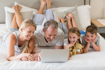 Parents with their kids lying on bed and using laptop in bedroomの写真素材