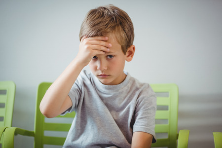 Portrait of upset boy sitting on chair in corridor at hospitalの写真素材