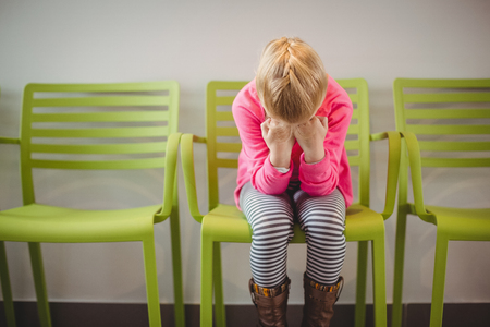 Upset girl sitting on chair in corridor at hospitalの写真素材