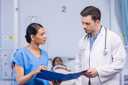 Nurse and doctor discussing over clipboard in hospital roomの写真素材
