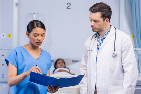 Nurse and doctor discussing over clipboard in hospital roomの写真素材
