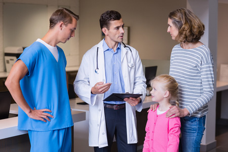 Doctors discussing medical report with mother and daughter in hospital corridorの写真素材