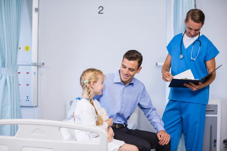 Smiling sick girl and father in hospital bedの写真素材