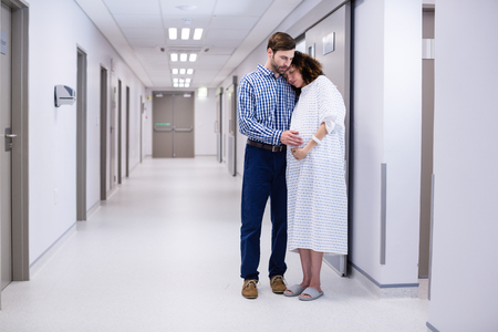 Man comforting pregnant woman in corridor of hospitalの写真素材