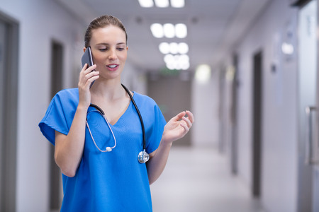 Female doctor talking on mobile phone in corridor of hospitalの写真素材
