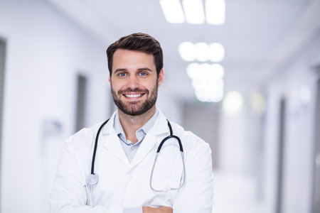 Portrait of male doctor standing with arms crossed in corridor of hospitalの写真素材