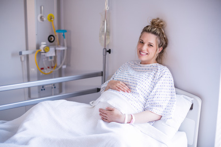Portrait of pregnant woman relaxing on hospital bed in wardの写真素材