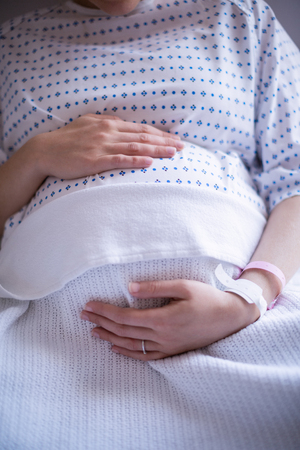 Mid section pregnant woman relaxing on hospital bed in wardの写真素材