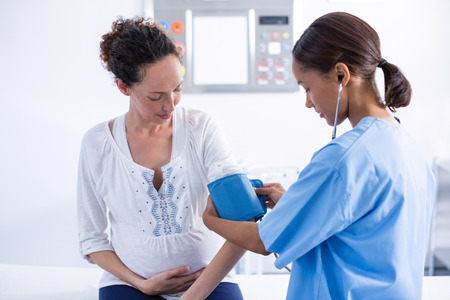 Doctor checking blood pressure of pregnant woman in hospitalの写真素材