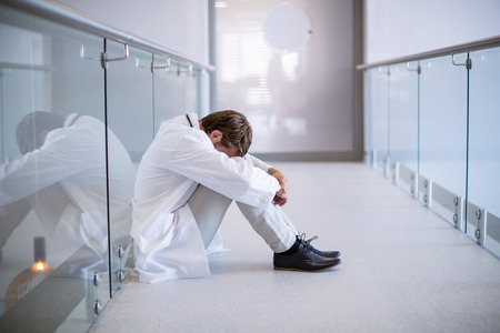 Tensed doctor sitting in corridor of hospitalの写真素材